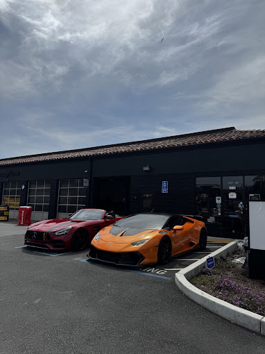 Two luxury sports cars parked outside a dark garage under cloudy skies