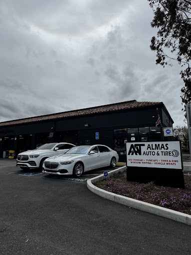 White luxury cars parked at Almas Auto & Tires under cloudy sky