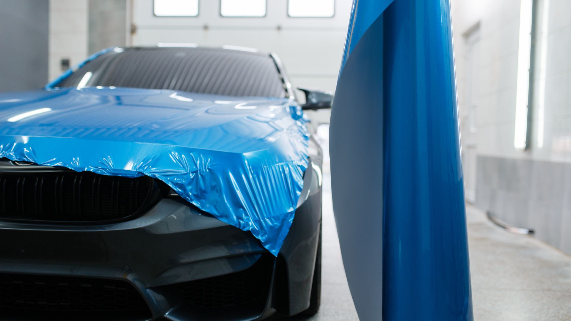 Blue car with protective film, partially wrapped in workshop