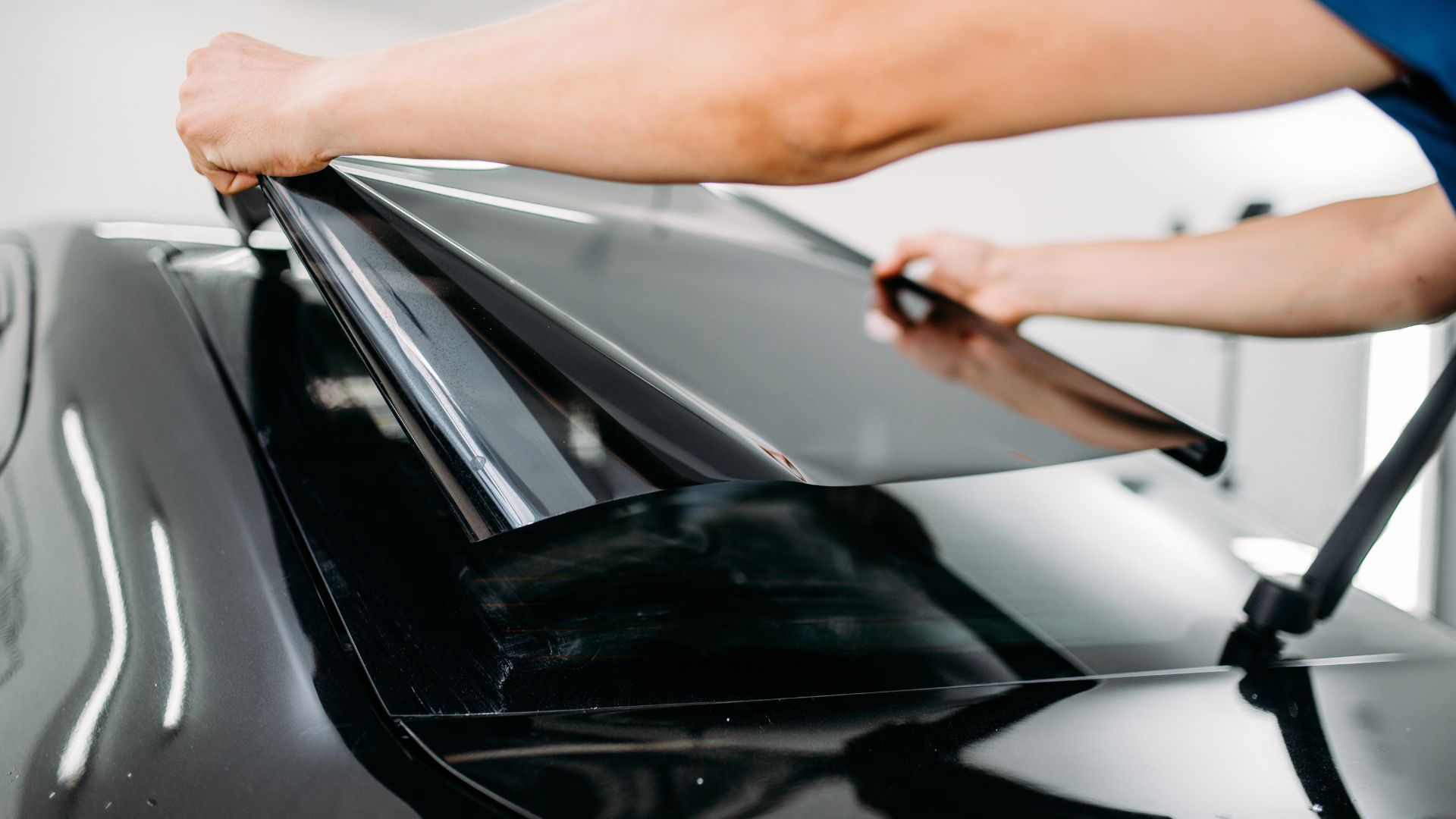 Worker applying window tint film to car window with professional tool
