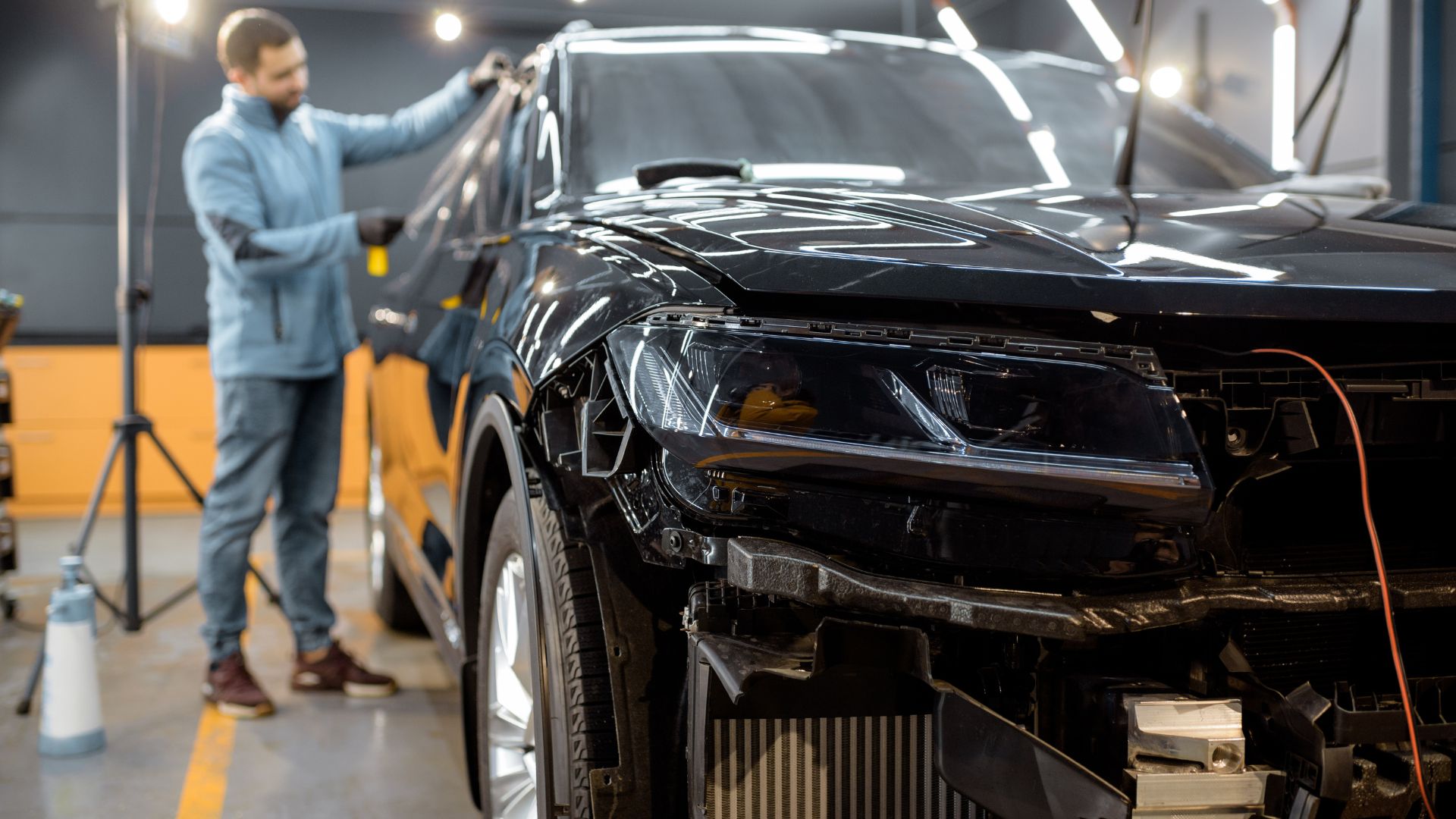 Black car being repaired in auto body shop with technician working