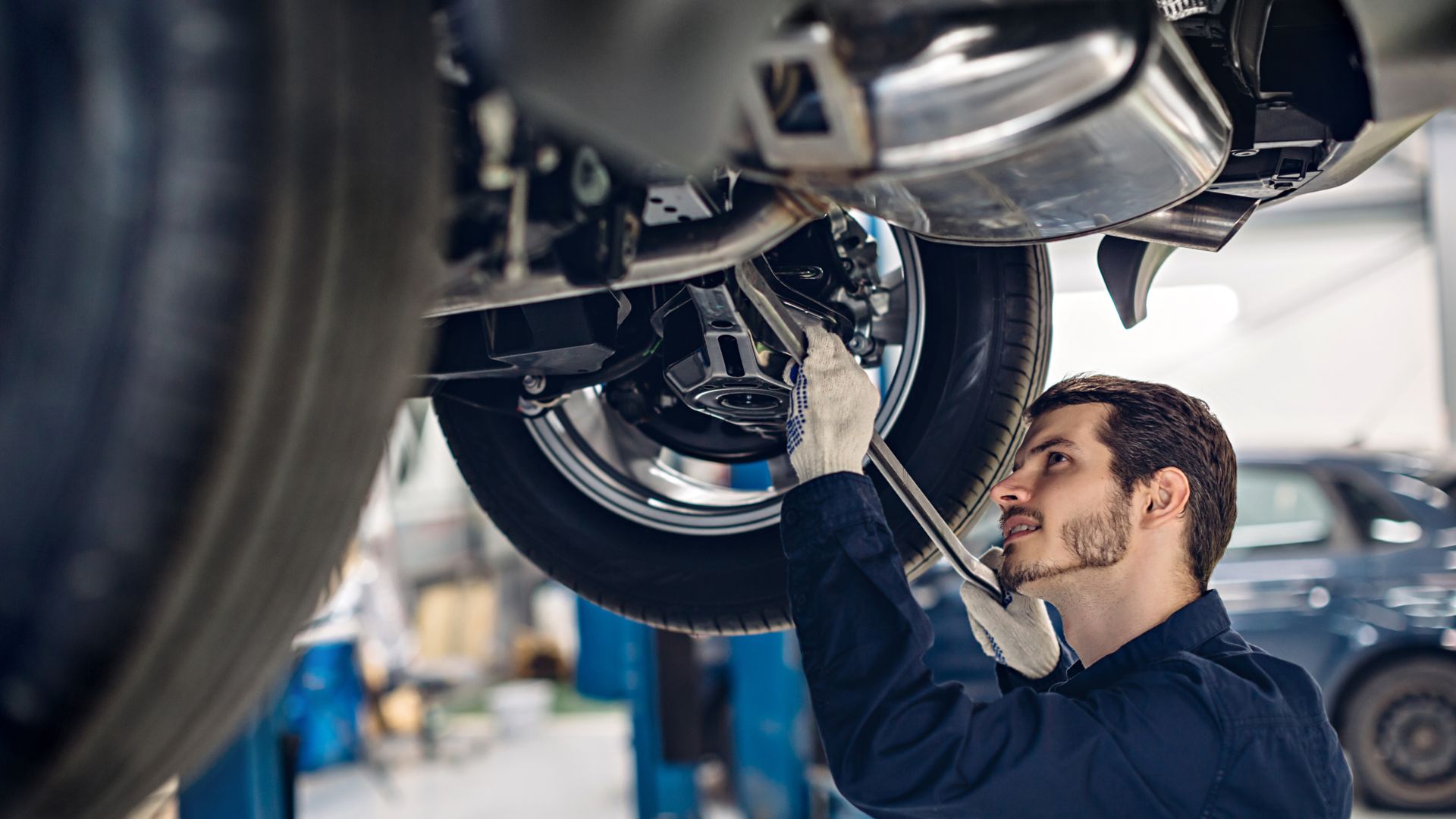 Mechanic inspecting car suspension and tire during automotive maintenance